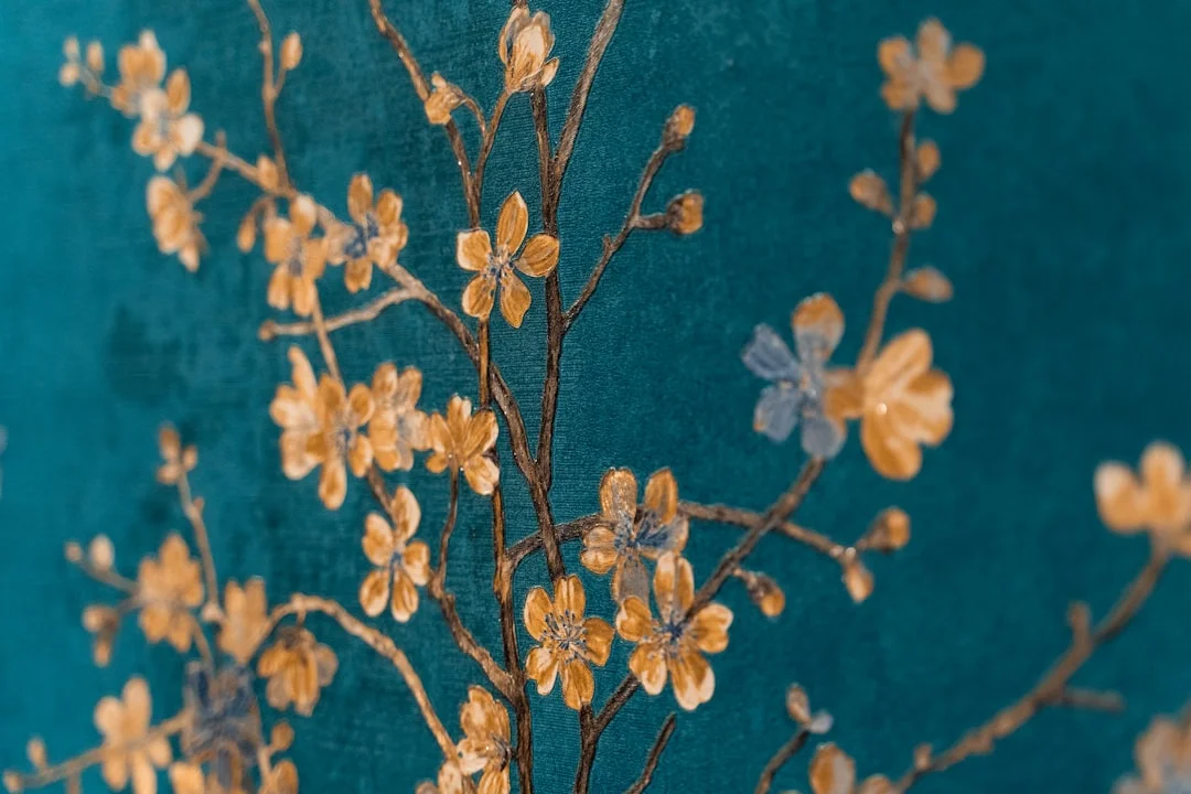 A sunlit living room with a dramatic floor-to-ceiling chinoiserie mural wallpaper in soft blues and greens behind a linen sofa, with paint samples and wallpaper swatches fanned out on a coffee table